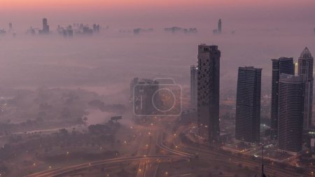 Téléchargez les photos : Big crossroad junction between JLT district and Dubai Marina intersected by Sheikh Zayed Road night to day transition aerial . Cars traffic covered by morning fog - en image libre de droit