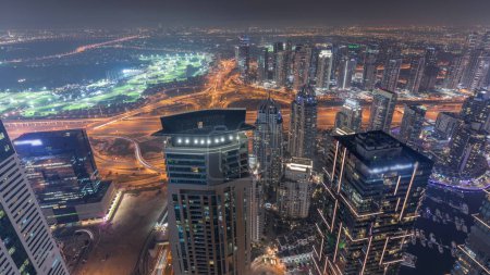 Téléchargez les photos : Panorama of Dubai Marina with JLT skyscrapers and golf course night , Dubai, United Arab Emirates. Aerial view from above towers. City lights illumination - en image libre de droit