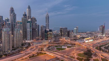 Téléchargez les photos : Panorama of Dubai Marina and media city highway intersection spaghetti junction day to night transition after sunset. Illuminated tallest skyscrapers on a background. Aerial top view from JLT district - en image libre de droit