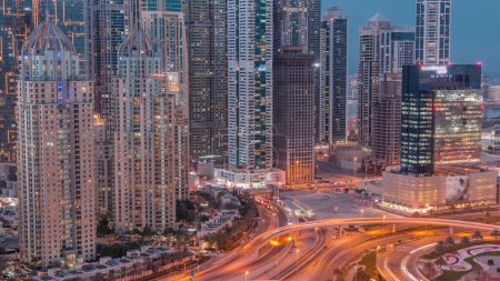 Foto de Skyscrapers of Dubai Marina with illuminated highest residential buildings day to night  after sunset. Aerial top view from JLT district with highway intersection - Imagen libre de derechos