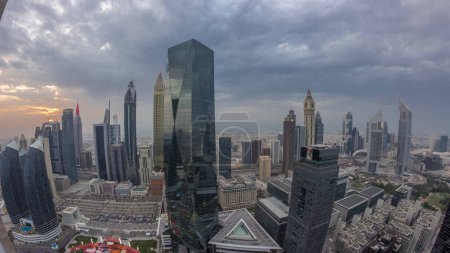 Foto de Panorama of futuristic skyscrapers with sunset in financial district business center in Dubai on Sheikh Zayed road . Aerial view from above with orange cloudy sky - Imagen libre de derechos