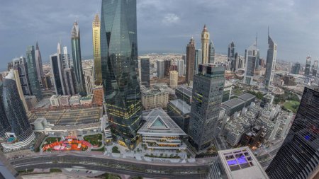 Téléchargez les photos : Panorama of futuristic skyscrapers in financial district business center in Dubai with road traffic night to day transition . Aerial view from above with illuminated towers during sunrise - en image libre de droit