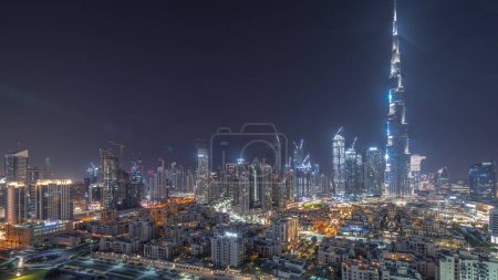 Téléchargez les photos : Dubai Downtown during all night with moon and lights turning off  with tallest skyscraper and other illuminated towers panoramic view from the top in Dubai, United Arab Emirates. - en image libre de droit
