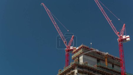 Foto de Edificio alto de varios pisos en construcción y grúas rojas. Trabajos activos en obras de construcción de una nueva torre - Imagen libre de derechos