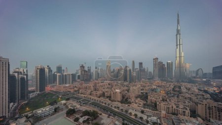 Téléchargez les photos : Dubai Transition du centre-ville de nuit au jour avec le plus haut gratte-ciel et d'autres tours avec une vue ombragée depuis le sommet pendant le lever du soleil, Émirats arabes unis. Maisons traditionnelles de la vieille ville - en image libre de droit