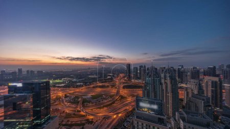 Téléchargez les photos : Énorme carrefour routier entre le quartier JLT et Dubai Marina croisé par Sheikh Zayed Road panoramique de nuit aérienne. Terrain de golf près des tours éclairées et des gratte-ciel avec un trafic achalandé - en image libre de droit
