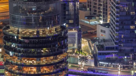 Téléchargez les photos : Dubai Marina front de mer et bâtiment avec différents restaurants à chaque étage aérien pendant toute la nuit. Creek, yachts avec jetée et gratte-ciel autour avec lumières éteintes - en image libre de droit