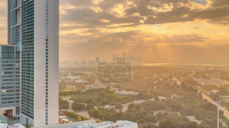 Foto de Sunrise over garden in Zabeel district with skyscrapers on a background aerial  in Dubai, UAE. Orange clouds on the sky with rays of sun light - Imagen libre de derechos