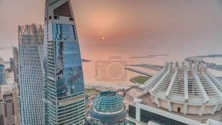 Téléchargez les photos : Aerial sunset view of JBR and Dubai Marina skyscrapers and luxury buildings  from above. Modern towers with beach and sun on orange sky reflected in sea - en image libre de droit