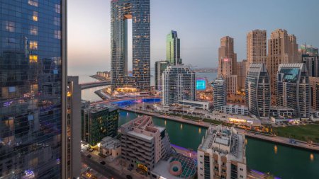 Foto de Dubai Marina rascacielos y el distrito JBR después de la puesta del sol con edificios de lujo iluminados y resorts día aéreo a la transición nocturna. Frente al mar con palmeras y barcos flotando en el canal - Imagen libre de derechos