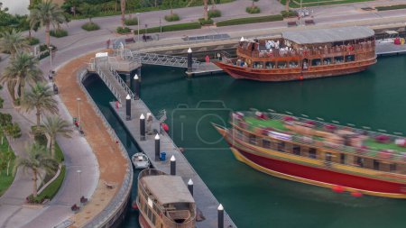Téléchargez les photos : Vieux bateau en bois près de la promenade au bord de l'eau avec palmiers et gazon vert aérien. Dhow croisière et jetée à Dubai Marina d'en haut, Émirats arabes unis - en image libre de droit