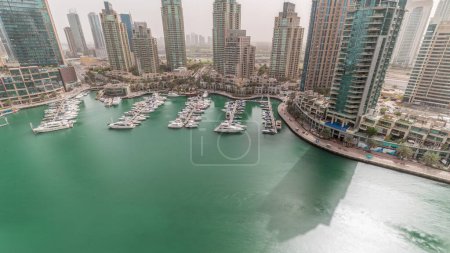 Téléchargez les photos : Baie de yacht de luxe dans le port de plaisance de Dubaï le matin après le lever du soleil avec de longues ombres se déplaçant rapidement. Des gratte-ciel modernes le long de la promenade riveraine et des bateaux flottant dans le port - en image libre de droit