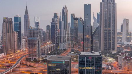 Photo for Panorama of Dubai Financial Center district with tall skyscrapers with illumination night to day transition . Aerial view to towers along busy highway before sunrise - Royalty Free Image
