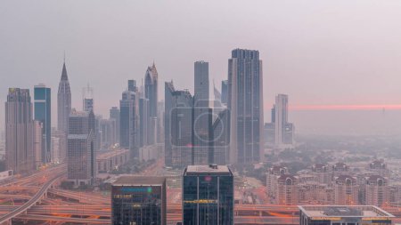 Photo for Panorama of Dubai Financial Center district with tall skyscrapers with illumination night to day transition . Aerial view to towers with morning fog before sunrise - Royalty Free Image
