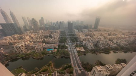 Photo for Sunrise over skyscrapers in Barsha Heights district and low rise buildings in Greens district aerial  look down view during all day. Dubai skyline with foggy weather and shadows moving fast - Royalty Free Image