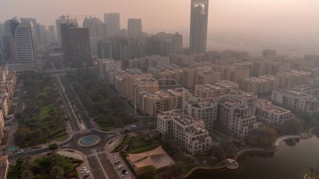 Téléchargez les photos : Des gratte-ciels dans le district de Barsha Heights et des immeubles de faible hauteur dans le district de Greens pendant le lever du soleil. Skyline de Dubaï avec ciel orange au matin brumeux - en image libre de droit