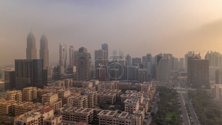 Téléchargez les photos : Skyscrapers in Barsha Heights district and low rise buildings in Greens district during sunrise with morning fog aerial . Dubai skyline with palms and trees - en image libre de droit