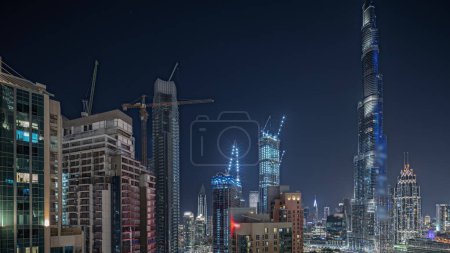 Téléchargez les photos : Panorama showing aerial cityscape night  with illuminated architecture of Dubai downtown. Many tall skyscrapers and towers with glowing windows. New construction site. - en image libre de droit