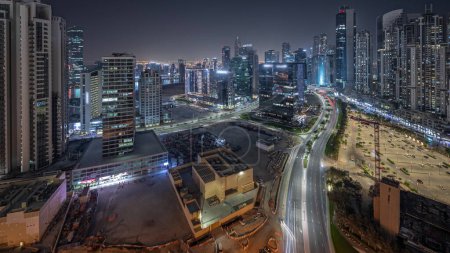 Photo for Panorama showing Bay Avenue with illuminated modern towers residential development in Business Bay aerial night , Dubai, UAE. Skyscrapers with traffic on a road near big parking lot - Royalty Free Image