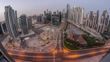 Foto de Panorama of Bay Avenue with modern towers residential development in Business Bay aerial night to day transition , Dubai, UAE. Skyscrapers with sunrise over big parking lot - Imagen libre de derechos