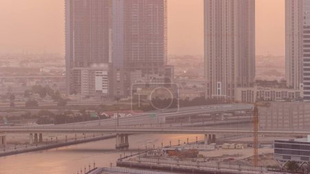 Téléchargez les photos : Paysage urbain gratte-ciel de Dubai Business Bay avec pont sur canal d'eau et ciel couchant aérien. Skyline moderne avec des tours en construction et front de mer. Un centre d'affaires international - en image libre de droit