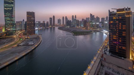 Téléchargez les photos : Paysage urbain de gratte-ciel à Dubai Business Bay avec canal d'eau aérien de jour comme de nuit transition panoramique. Skyline moderne avec tours et front de mer après le coucher du soleil. Un centre d'affaires international - en image libre de droit