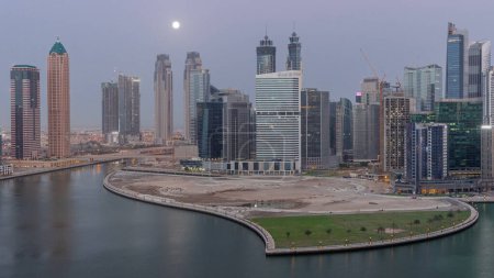 Téléchargez les photos : Cityscape of skyscrapers in Dubai Business Bay with peninsula on water canal aerial night to day transition with Moon setting down. Modern skyline with illuminated towers and waterfront before sunrise - en image libre de droit