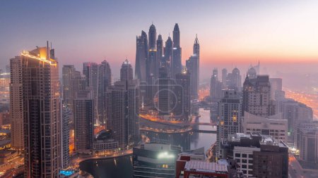 Foto de View of various skyscrapers in tallest recidential block in Dubai Marina aerial night to day transition  with artificial canal. Many towers and yachts foggy morning before sunrise - Imagen libre de derechos