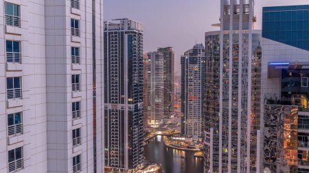 Téléchargez les photos : Grands bâtiments résidentiels du quartier JLT transition aérienne du jour à la nuit, faisant partie du quartier mixte du centre multi-commodités de Dubaï. Tours lumineuses avec fenêtres éclatantes - en image libre de droit
