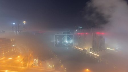 Photo for Modern city architecture in Business bay district during all night. Panoramic aerial view of Dubai's illuminated skyscrapers  with traffic on the road. Foggy weather and sunrise - Royalty Free Image