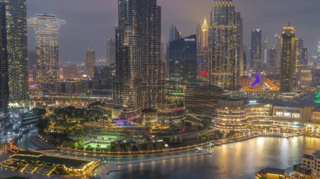 Téléchargez les photos : Gratte-ciel s'élevant au-dessus du centre-ville de Dubaï transition de jour à la nuit, centre commercial et fontaine entourés de bâtiments modernes vue aérienne avec ciel nuageux coloré - en image libre de droit