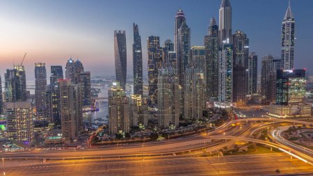 Téléchargez les photos : Gratte-ciel de Dubai Marina avec les bâtiments résidentiels les plus lumineux transition de jour à la nuit après le coucher du soleil avec la circulation sur une autoroute. Vue aérienne du quartier JLT - en image libre de droit