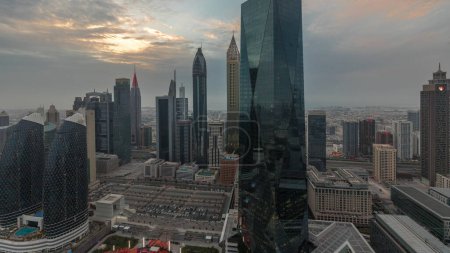 Foto de Puesta de sol sobre el centro financiero de la ciudad de Dubai con rascacielos de lujo, Dubai, Emiratos Árabes Unidos. Vista panorámica aérea con cielo naranja y torres alrededor de gran estacionamiento - Imagen libre de derechos