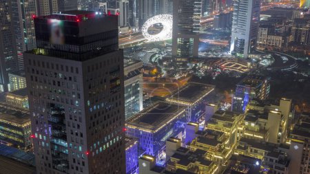 Photo for Office tower with glowing windows located in the Dubai International Financial Centre night . Dubais central financial district aerial view with traffic on a circle road - Royalty Free Image