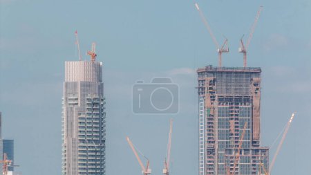 Téléchargez les photos : Bâtiments hauts de plusieurs étages en construction contre ciel nuageux bleu et de nombreuses grues. Travaux actifs sur le chantier de construction de nouveaux gratte-ciels et tours - en image libre de droit