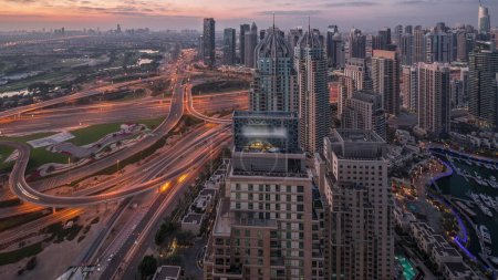 Foto de Dubai marina and JLT illuminated skyscrapers along Sheikh Zayed Road with traffic on big junction aerial night to day transition  before sunrise. Residential and office buildings from above. - Imagen libre de derechos