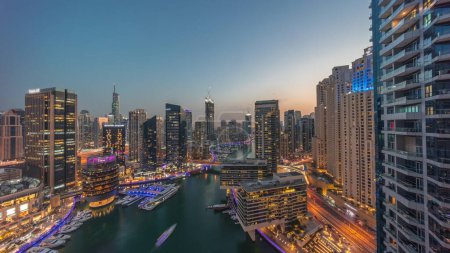 Téléchargez les photos : Vue aérienne panoramique sur les gratte-ciel de la marina de Dubaï autour du canal avec des bateaux flottants transition jour-nuit. Les bateaux blancs sont garés dans le yacht club après le coucher du soleil - en image libre de droit