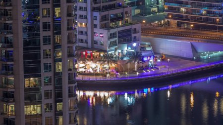 Foto de Vista aérea de Dubai Marina rascacielos iluminados y muchos restaurantes de noche. Torres a lo largo de la zona de paseo en un paseo marítimo. Dubai, Emiratos Árabes Unidos - Imagen libre de derechos