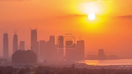 Photo for Sunrise over Dubai Creek Harbor with skyscrapers and towers under construction aerial . Big red Sun rise up behind buildings - Royalty Free Image