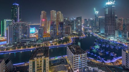 Foto de Dubai Marina con barcos y yates estacionados en el puerto y rascacielos iluminados alrededor del canal panorámico aéreo durante toda la noche. Torres del distrito JBR en segundo plano - Imagen libre de derechos