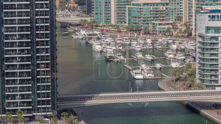 Téléchargez les photos : De nombreux yachts et bateaux sont garés dans l'antenne du port toute la journée avec des ombres se déplaçant rapidement. Dubai Marina front de mer zone de marche. Bateau moderne est sur le ruisseau. - en image libre de droit