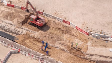 Téléchargez les photos : Groupe de travailleurs et excavatrice rouge creusant le drainage de l'eau sur le chantier de construction vue aérienne de près. Réparation de tuyaux - en image libre de droit