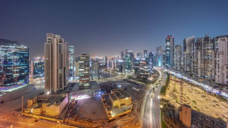 Téléchargez les photos : Business Bay with modern towers residential development aerial panoramic day to night transition , Dubai, UAE. Skyscrapers with traffic on a road near big parking lot after sunset - en image libre de droit