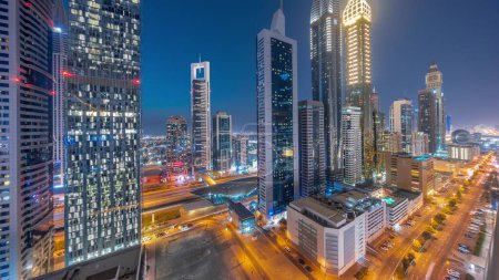 Photo for Aerial panorama of Dubai International Financial District with many skyscrapers night after sunset. Traffic on a road near multi storey parking with rooftop swimming pool. Dubai, UAE. - Royalty Free Image
