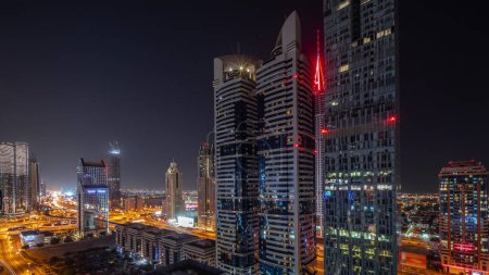 Foto de Vista aérea del Distrito Financiero Internacional de Dubái con muchos rascacielos durante toda la noche. Tráfico en un cruce de carreteras rodeado de torres iluminadas con luces apagadas. Dubai, Emiratos Árabes Unidos. - Imagen libre de derechos