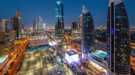 Foto de Vista panorámica aérea del Distrito Financiero Internacional de Dubái con muchos rascacielos noche después del atardecer. Tráfico en una carretera cerca de estacionamiento en la zona de paseo avenida comercial. Dubai, Emiratos Árabes Unidos. - Imagen libre de derechos