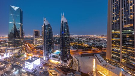Foto de Vista aérea del Distrito Financiero Internacional de Dubái con muchos rascacielos panorámicos de transición día a noche después del atardecer. Tráfico en carreteras cerca de la avenida comercial con zona de paseo en la azotea. Dubai, Emiratos Árabes Unidos. - Imagen libre de derechos