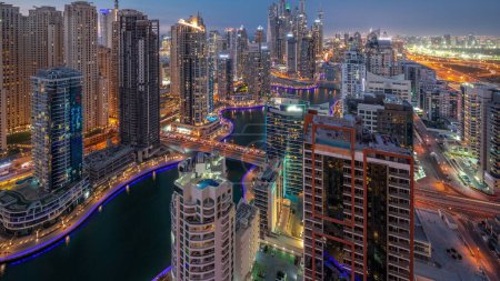 Téléchargez les photos : Vue de divers gratte-ciel dans le plus haut bloc recidential de Dubai Marina transition aérienne de jour à la nuit avec canal artificiel et des ponts au-dessus. Nombreuses tours et yachts après le coucher du soleil - en image libre de droit