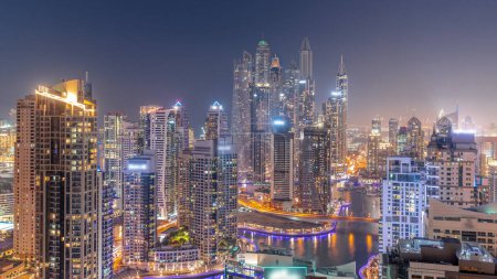 Téléchargez les photos : View of various skyscrapers in tallest recidential block in Dubai Marina aerial day to night transition panoramic  with artificial canal. Many towers and yachts after sunset - en image libre de droit