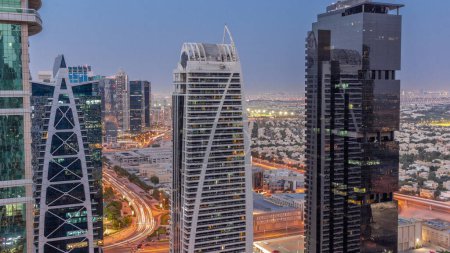 Foto de Edificios residenciales altos en el distrito JLT transición aérea día a noche, parte del distrito de uso mixto del centro de productos básicos de Dubai. Casas de villas y tráfico por carretera en un segundo plano - Imagen libre de derechos
